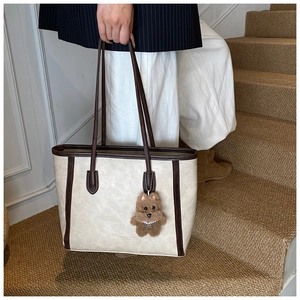Close-up of large tote bag with bear charm and golden logo on off-white leather