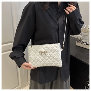 Close-up of a white quilted crossbody bag featuring a delicate gold bow accent