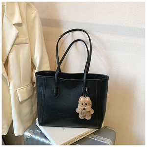 Détail du sac cabas en cuir noir avec logo de marque et pendentif chien en peluche marron