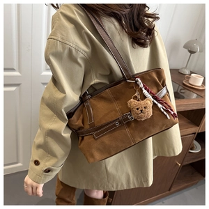 Detailed shot of brown suede tote bag with leather trim and bear pendant charm