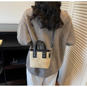 Chic beige bucket bag with black leather trim worn as a crossbody in a stylish setting