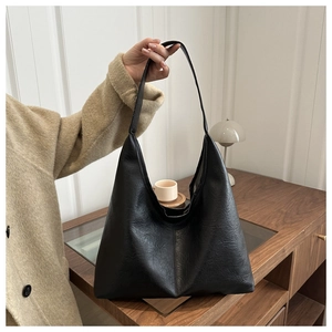 Detail of soft black leather tote bag with wide strap in a minimalist lifestyle setting