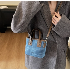 Detail of teal canvas bucket bag with brown handles and gold rivets on a grey blazer