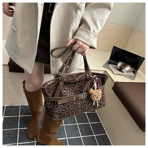 Detail of leopard print tote bag with brown leather handles and a plush bear pendant