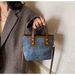 Detail of a denim blue tote bag with brown leather straps and metal rivets on gray blazer