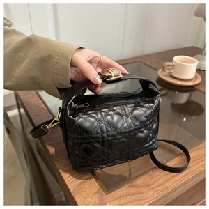 Détail du sac seau noir à matelassage cœur avec garniture dorée dans un café chic
