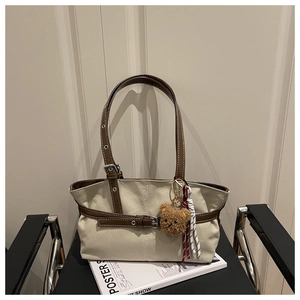 Dettaglio borsa sottobraccio in tela beige con cinturini in pelle marrone e ciondolo orsetto