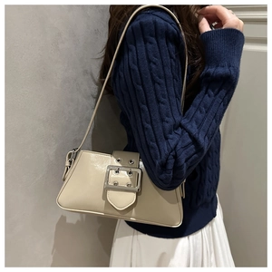 Détail d'un sac baguette crème avec boucle argentée porté sur un pull bleu et jupe blanche