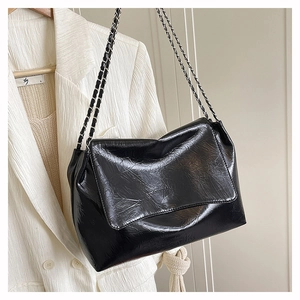 Détail d'un sac noir brillant à chaîne porté sur un costume blanc texturé chic