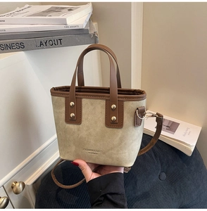 Detail of canvas bucket bag showing leather trim, rivets and logo on beige fabric