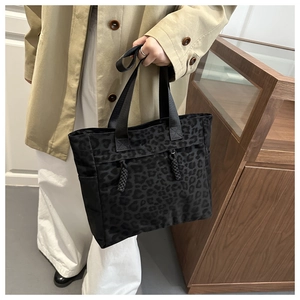 Detail of black leopard print tote bag with woven straps and side pockets on wooden background