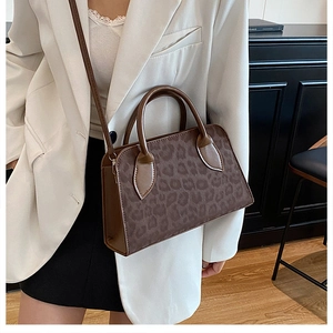 Close-up of a leopard print tote bag with brown leather handles worn by a model