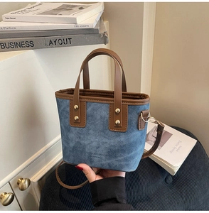 Detail of blue denim mini tote bag with brown leather trim and golden rivet accents