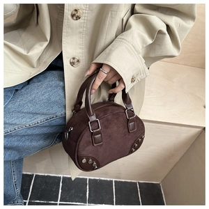 Detail of brown suede shell bag with silver rivets held by model in beige trench coat