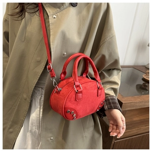 Detail of red suede boston bag with silver rivets worn by a model in a trench coat