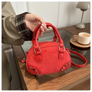 Detailed view of red shell bag with silver rivets and dual handles on a wooden table