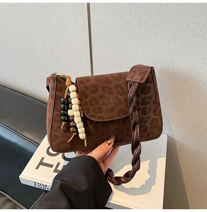 Detail of leopard print crossbody bag with tassel charm and woven handle on a white book