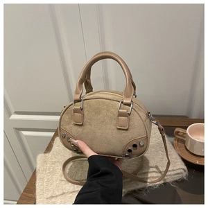 Detailed view of beige suede bowling bag with silver studs on a cozy textured background
