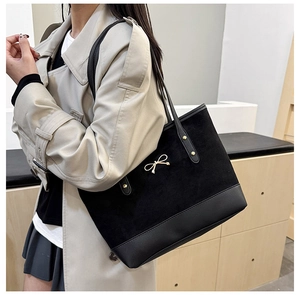 Détail d'un grand sac cabas noir avec un nœud doré et un mélange de textures daim-cuir