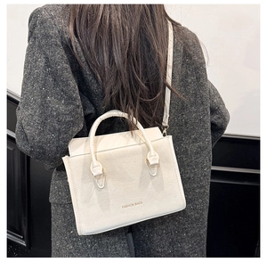 Détail d'un sac à main beige minimaliste en similicuir texturé sur une tenue grise