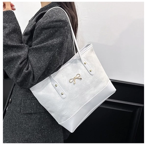 Détail du sac cabas blanc montrant le nœud doré et la texture du tissu sur l'épaule