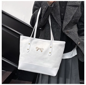 Détail du sac cabas blanc avec nœud doré et rivets sur une texture de type daim chic
