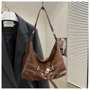 Close-up of brown glossy PU leather crescent bag with silver buckles and metal eyelets