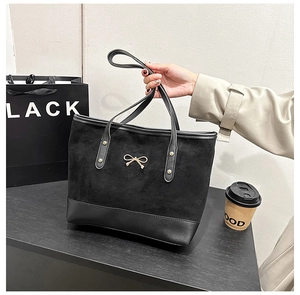 Détail du sac fourre-tout en daim noir orné d'une boucle métallique en nœud doré