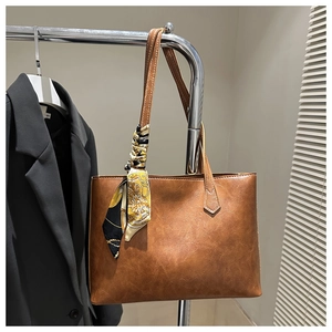 Brown leather tote bag with a patterned silk scarf handle detail hanging on a rack