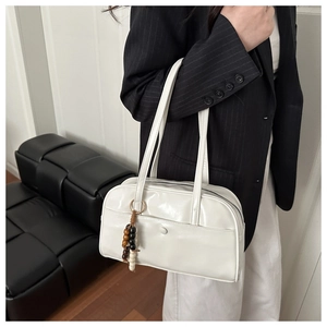 Detail of white glossy pillow bag featuring stylish beaded charm and sleek handle