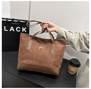 Détail du sac cabas en daim marron chaud avec lanières en cuir et nœud doré élégant