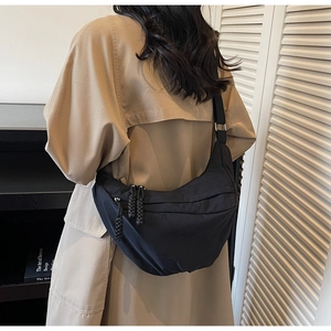 Detailed view of a black nylon crescent bag worn over a khaki trench coat