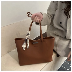 Dettaglio della borsa tote in pelle marrone con barra metallica argentata e foulard