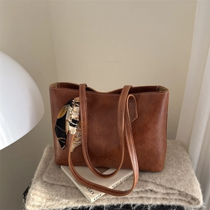 Large dark brown tote bag with vintage texture and silk scarf accessory on soft background