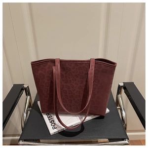 Detail of dark red leopard print tote bag on a modern chair with artistic magazine
