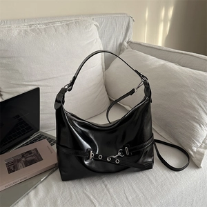 Retro black glossy leather hobo bag with silver buckle and chain on white sofa