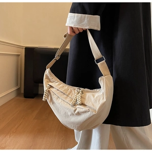 Adjustable beige nylon crescent crossbody bag styled by a model in an indoor setting