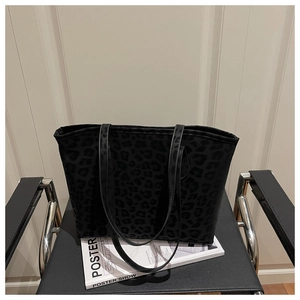 Close-up of black leopard print suede tote bag placed on a sleek black leather chair