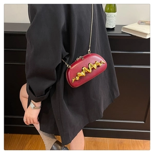 Detail of burgundy leather semi-circle crossbody bag with gold metal wave decoration