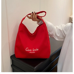 Detail of red canvas hobo tote featuring white C'est la vie text on a black cabinet