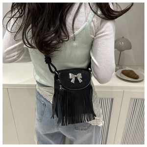 Detail of black crossbody bag featuring silver bow accent and long fringe tassels
