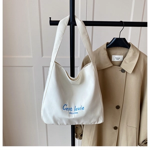 Detailed view of white canvas tote bag with blue C'est la vie embroidery and wide strap