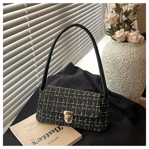 Dettaglio borsa a tracolla in tweed nero con chiusura in metallo dorato su sfondo