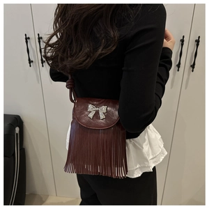 Macro detail of wine red leather crossbody bag with silver bow and long tassels