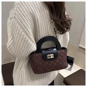 Detail of quilted brown fabric handbag with black leather handle and gold twist lock