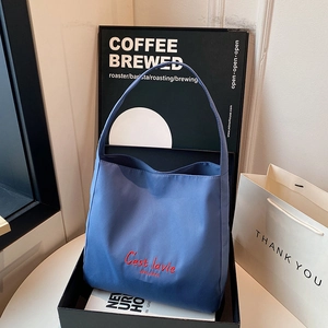 Blue tote bag with red C'est lavie embroidery in a luxury gift display setting