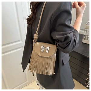 Close-up of beige crossbody bag with silver bow hardware and long fringe tassels