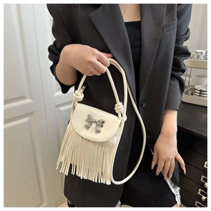 Detail of a white crossbody bag with silver bow ornament and long flowing fringe