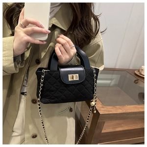 Detail of black quilted crossbody bag with golden twist lock and chain strap on model