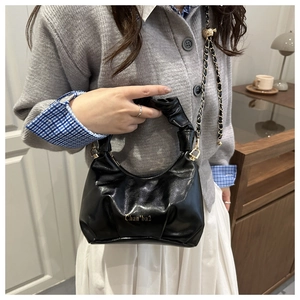 Détail du sac à main noir brillant avec poignée plissée et lettrage doré de marque